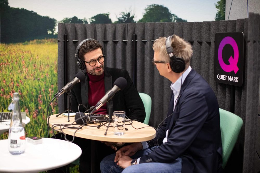 Two people recording a podcast with the Quiet Mark logo at the back