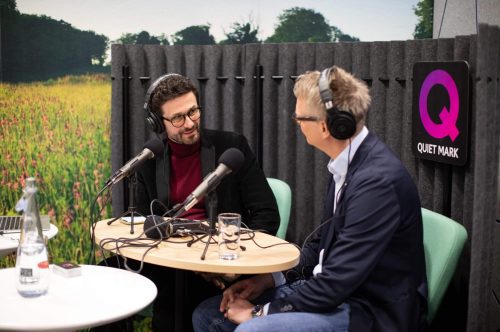 Two people recording a podcast with the Quiet Mark logo at the back