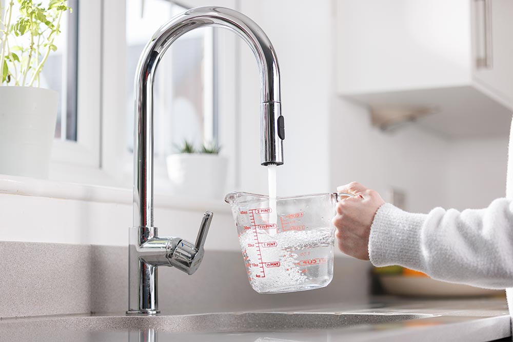 Someone filling up a measuring jug with water using the kitchen tap