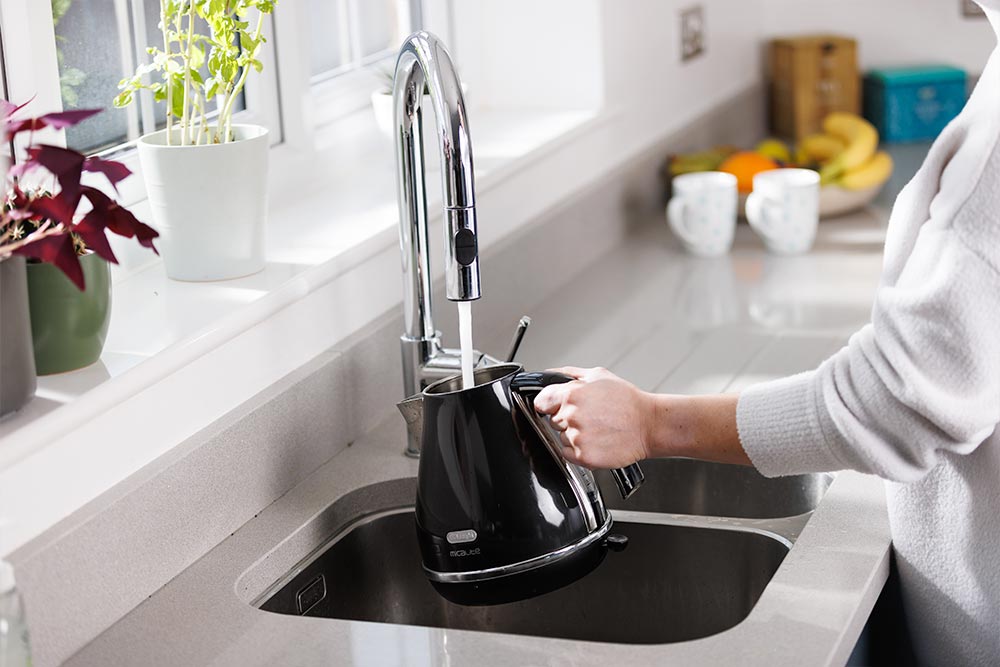 A kettle being filled up using the kitchen sink