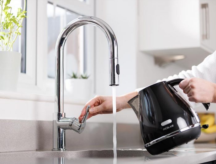 A person about to fill up a black kettle using the kitchen tap