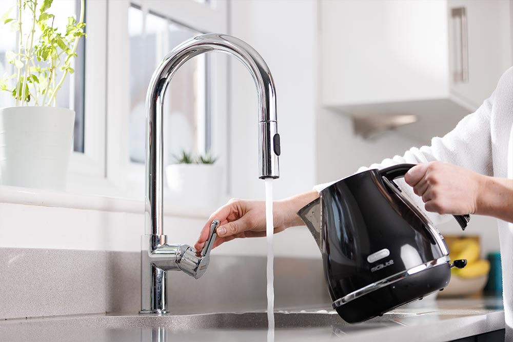 A person about to fill up a black kettle using the kitchen tap